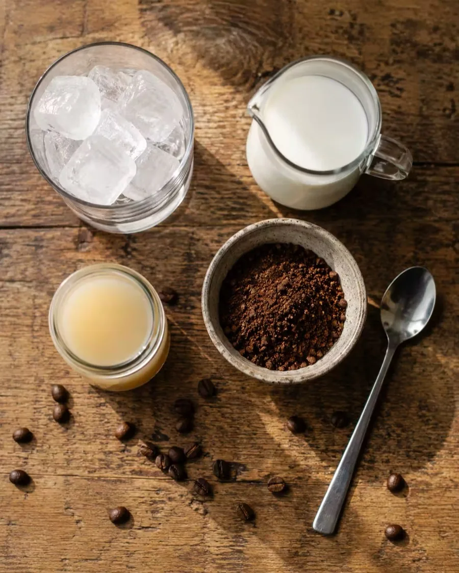 Glaçons, lait, café moulu et sirop disposés sur une table en bois, les ingrédients du café glacé maison